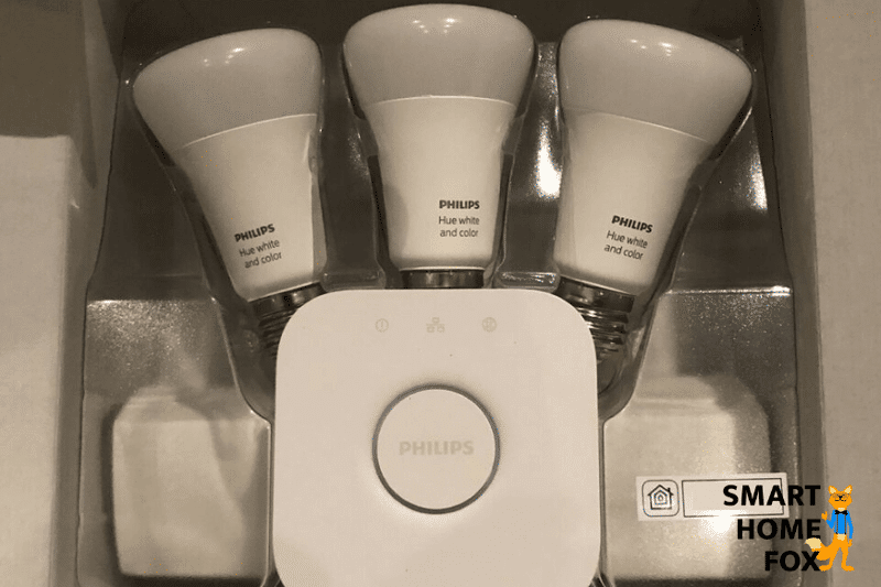 Man sieht eine Philips Hue Bridge mit Hue Leuchtelementen im Hintergrund.